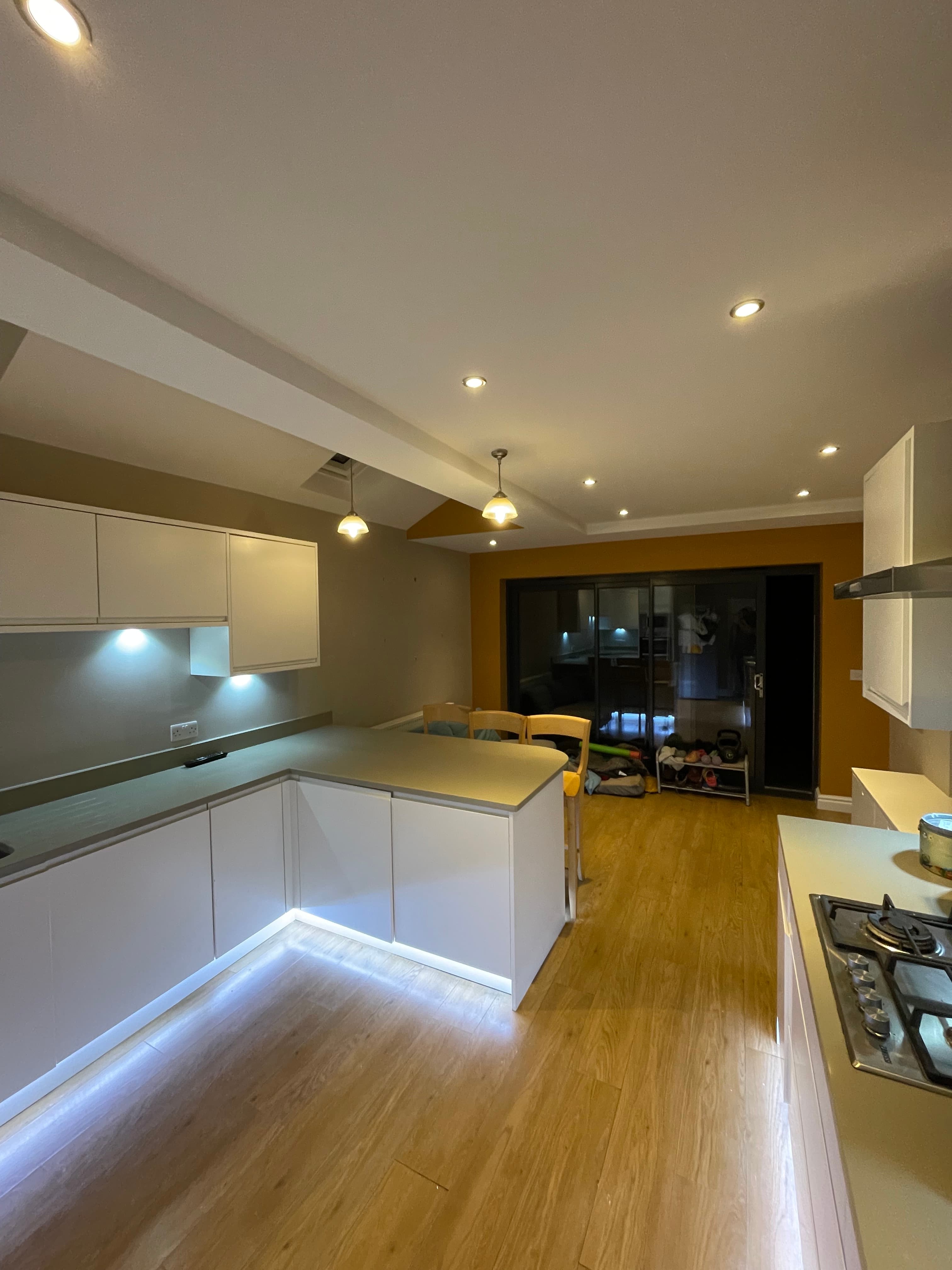 Modern kitchen featuring white cabinets, an illuminated island, wooden flooring, and recessed ceiling lighting.